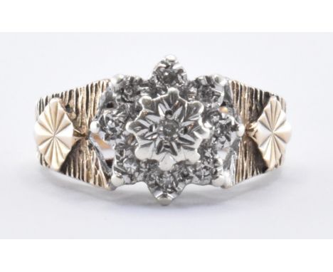 A 9ct gold and diamond cluster ring being illusion set with nine round cut diamonds. The ring having textured shoulders. Mark