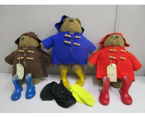 A group of three Paddington teddy bears, two with hand written luggage labels attached to the coats, red, yellow and blue Wel