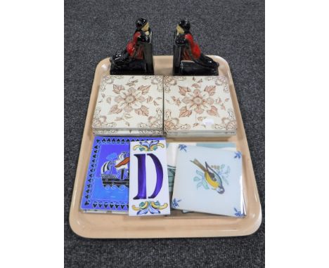 A tray containing a pair of early 20th century china bookends together with eleven Victorian and later ceramic tiles
