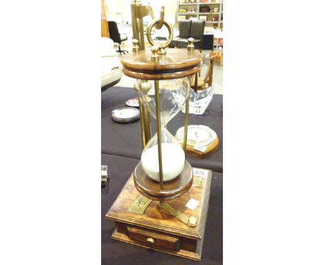 UNUSUAL HOUR GLASS. Unusual wood brass and glass hour glass timer with brass calendar, set on wood base with drawers