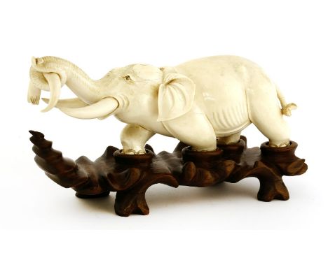 An ivory carving,19th century, of an elephant marching forward with a tusk in his trunk, 27cm long, wood stand (2)Provenance: