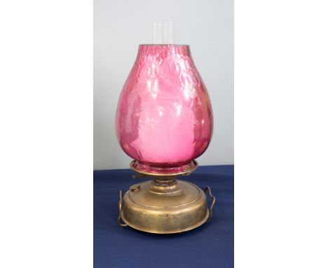 A Victorian oil lamp with a cranberry/pink coloured reservoir with a pink shade, height excluding chimney 43cm.