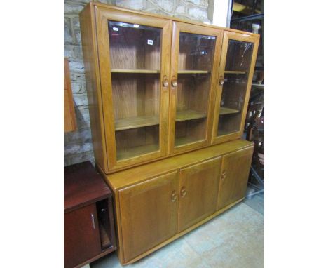 Ercol light elm dresser, the raised back with three glass fronted doors enclosing a shelved interior over abase fitted with t