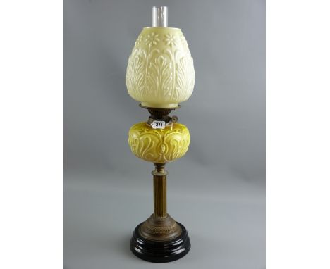 A Victorian oil lamp with relief moulded glass font on a brass column and black pottery base having a leaf and floral moulded