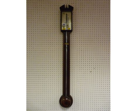 An antique mahogany stick barometer, pediment top with brass urn central finial, glazed opening door before a silvered dial m