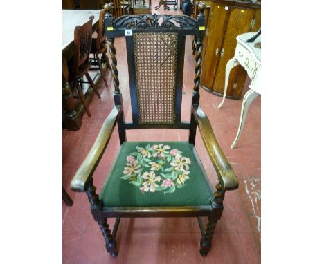 An oak barley twist armchair with crown carved top rail and cane work back, front barley twist supports and tapestry covered 