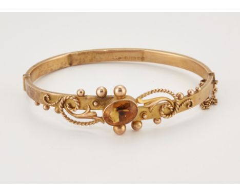 A VICTORIAN 9 CARAT GOLD CITRINE BANGLE, an oval-cut citrine to a fancy rope scroll and beaded hinge opening bangle. Hallmark