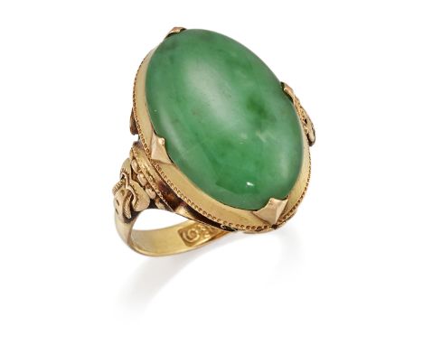 A JADE RING,&nbsp;an oval jade in a claw setting, to fancy buckle strap shoulders and a scrolling under-bezel. Marked '9', wi