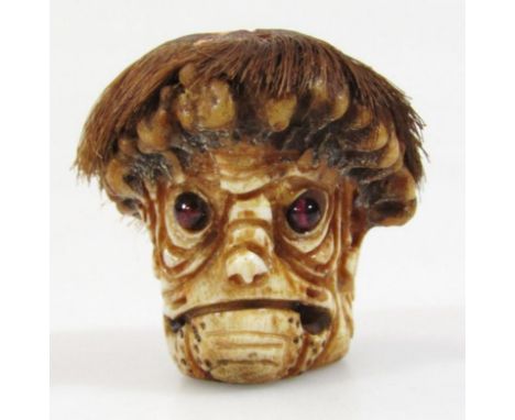 A 19thC Japanese netsuke, formed as a face with realistic hair, the eyes picked out in red with gruesome expression on oval b