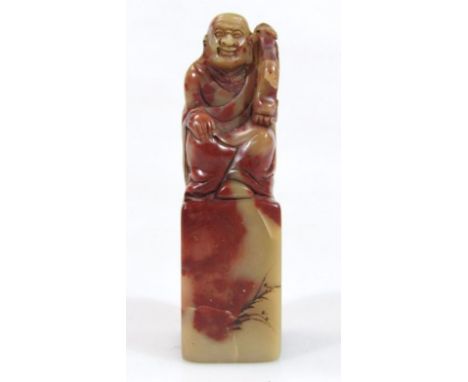 A Chinese Qing style soapstone desk seal figure, formed as a seated gentleman in flowing robes, holding sceptre, on a block b