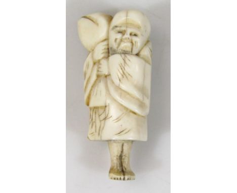 A Japanese Meiji period ivory netsuke, formed as a standing figure holding an enlarged Lotus flower, with two pierced holes v