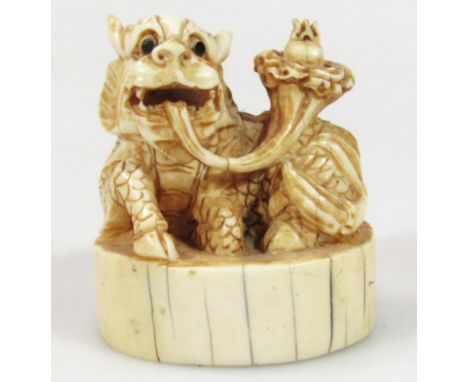 A 19thC Japanese ivory Meiji period netsuke, formed as a dragon in seated position with tongue out, on circular foot, carved 
