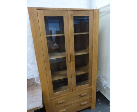 A modern light oak bookcase, two glazed doors over two drawers, on bracket feet
