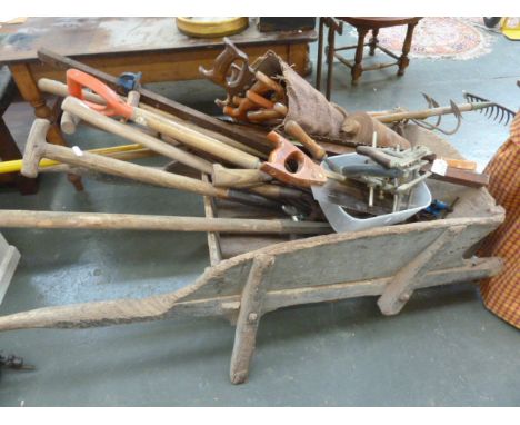 A vintage wooden wheelbarrow with a selection of vintage tools, including double saw, forks etc