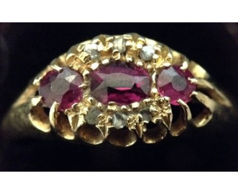 A ruby and diamond cluster ring, central oval pink ruby, flanked to each end by a round cut ruby, wrapped within arches of th