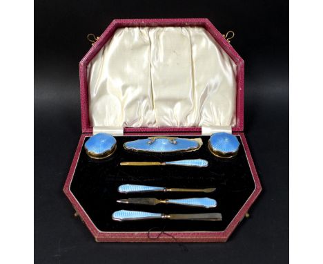 A cased silver dressing table set, serpentine edge lid with silver gilt and blue enamel decoration, missing scissors, marked 