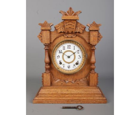 An early Twentieth Century oak cased Ansonia mantle clock, with carved detailing and twin spindle pillar decoration. Featurin