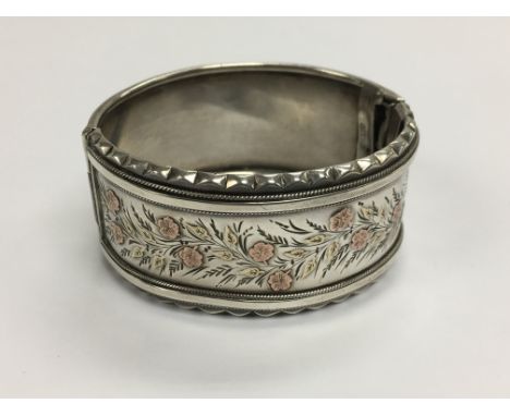 A silver bangle with rose and yellow coloured floral decoration.