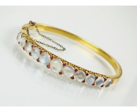 A late 19th century moonstone and ruby hinged bangle, designed as a row of eleven graduated round cabochon moonstones claw se