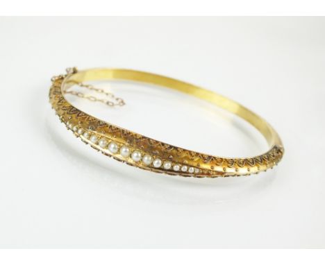 A late 19th century seed pearl bangle, designed as a central row of seventeen graduated split seed pearls, set within bead wo
