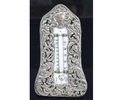 An Edwardian easel desk thermometer, the central scale within a silver clad surround with floral and C-scrolling decoration o