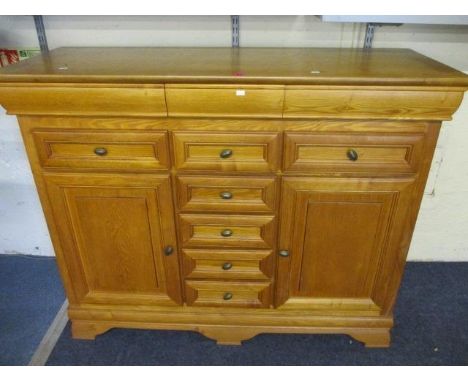 A modern light oak sideboard having five small central drawers flanked by two smaller drawers and two cupboards, to include a