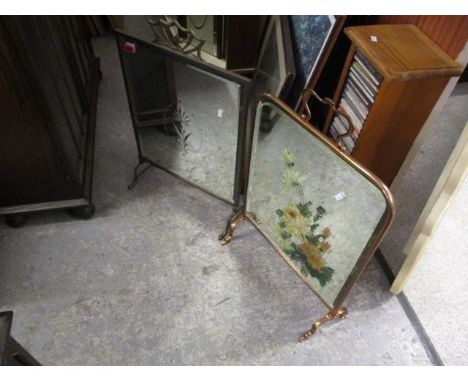 A copper mirrored firescreen with a flower decoration, together with a brass mirrored firescreen having etched decoration to 