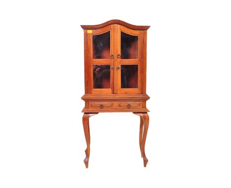 A 20th century mahogany cabinet on stand having bowed pediment top over twin glazed doors with ring handles, raised over cabr