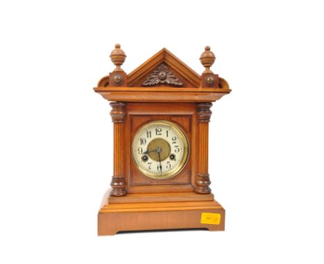 A Victorian eight day mahogany mantel clock. Having a triangular top decorated middle flanked by finials. With white face and