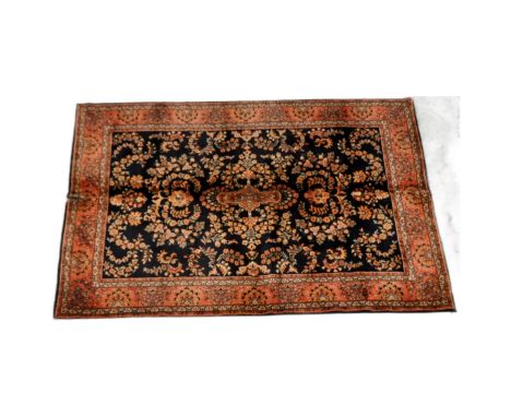 An early 20th Century Persian floor carpet rug. Central black ground with repeating floral motifs surrounded by red ground bo
