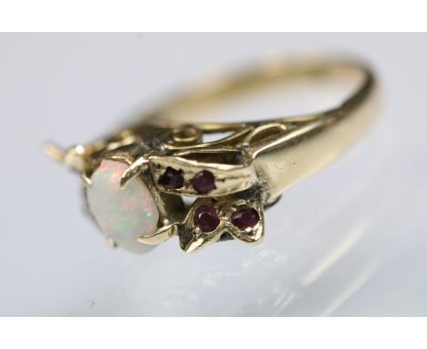 Opal and ruby dress ring set with an oval opal cabochon to centre surrounded by ruby accent stones within a foliate mount. Un