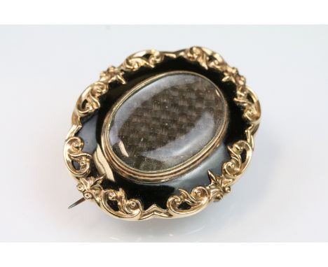 19th Century Victorian mourning brooch having a central oval hairwork panel within a raised scrolled border with black enamel