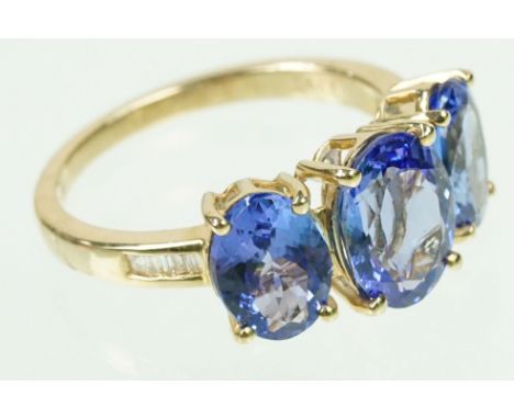 14ct gold and tanzanite three stone ring. The ring being set with three oval cut tanzanites with diamond accent stones to the