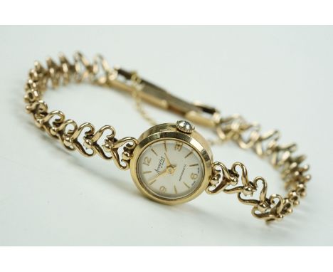 9ct gold Accurist wrist watch having a round face with baton markings to the chapter ring set to a 9ct gold heart link bracel