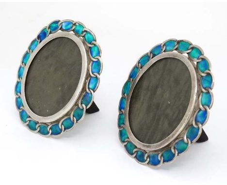 A pair of late 20thC white metal photograph frames of oval form with easel back and  with enamel decoration. 4 1/4" high  CON