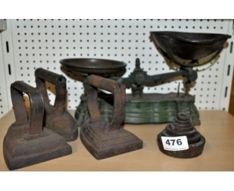 A kitchen scale and weights with three flat irons.