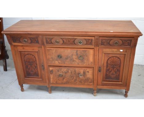 A 20th century walnut sideboard with three central drawers and two heavily carved cupboard doors to either side on small balu