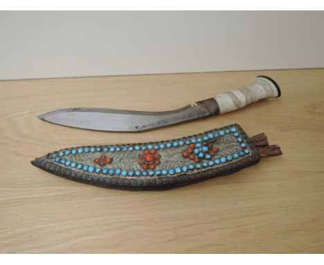 A Kukri Knife having decorated bone handle, blade slightly decorated, beaded and wire decorated scabbard with two small knive