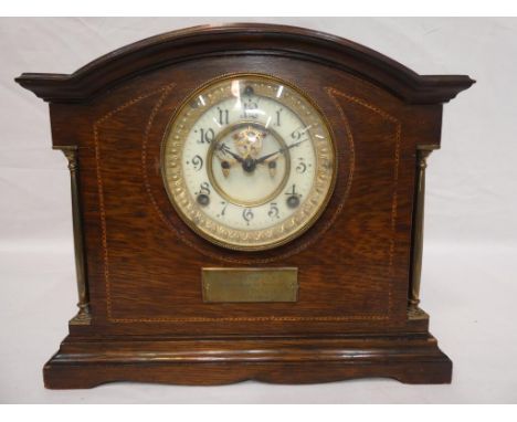 A mahogany and inlaid case mantel clock with visible escapement movement by Ansonia behind the white dial, presentation plaqu