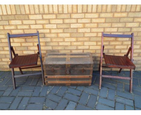A wooden and metal travel trunk with two fold away chairs.
