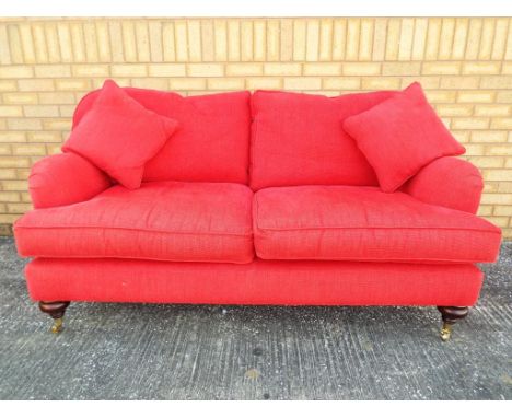 A two seater red upholstered sofa set on casters, approximate height 90 cm x 170 cm x 90 cm. 