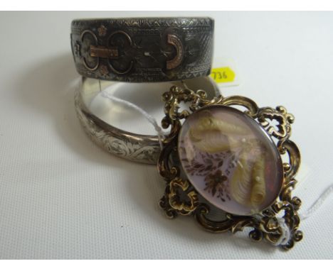 A bright-cut silver and yellow metal mounted clasp bangle, 36gms; and another, 25gms; together with a yellow metal scroll-fra