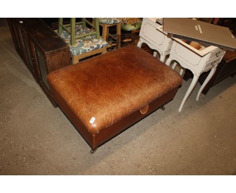 A tanned leather upholstered pouffe terminating on brass castors