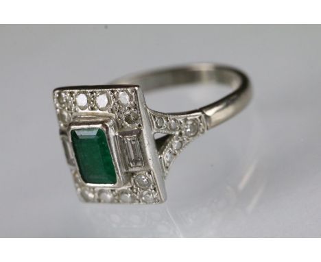 18ct white gold, emerald and diamond panel ring. The ring being set with a rectangular cut emerald to centre surrounded by ro