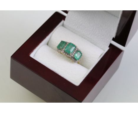 14ct gold, emerald and diamond three stone ring. The ring being set with three graduating emerald cut emeralds surrounded by 