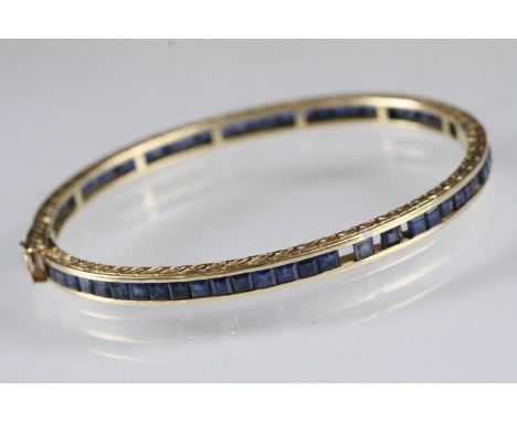 14ct gold and sapphire bangle bracelet channel set throughout with square step it sapphires. Hinged opening with safety clasp