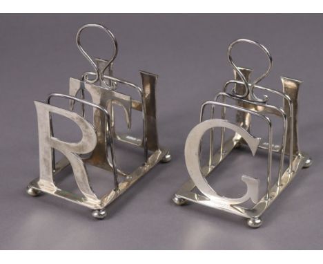 A pair of Edwardian silver novelty four-division toast racks, one with dividers formed from the capital letters RTH, the othe