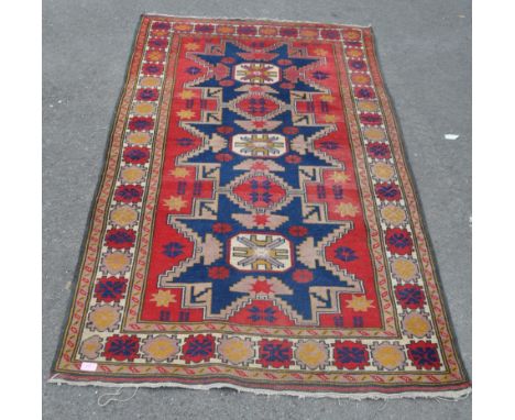 An early 20th century Kazak woollen floor carpet rug. Geometric medallions to centre in red and blue ground within a beige bo