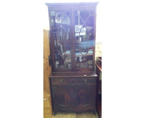 A George III style bookcase on cupboard, having a pair of bar glazed doors above a frieze drawer, with a pair of panel doors 