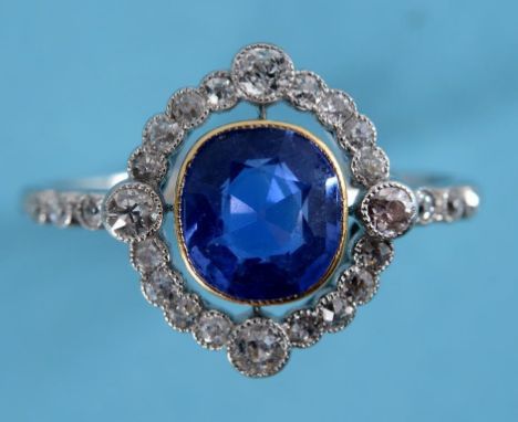 A white coloured metal, sapphire and diamond ring, the central cushion cut sapphire within a diamond halo and diamond set sho